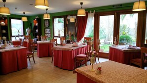 Un espace repas comprenant plusieurs tables dressées, chacune avec des chaises, et une grande fenêtre offrant une vue sur l’extérieur.