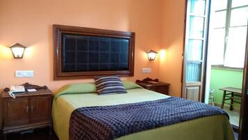 Habitación de hotel con una cama grande, dos mesitas de noche, una lámpara de pared y un ventanal con cortinas.