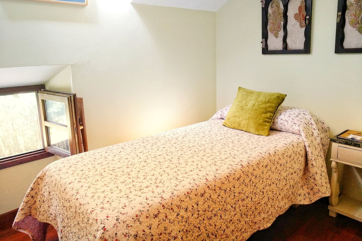Une chambre à coucher avec un lit, une table de chevet, une fenêtre et un mur orné de tableaux.
