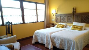 Une chambre d’hôtel avec deux lits, une chaise, une table de chevet et une fenêtre avec des rideaux.