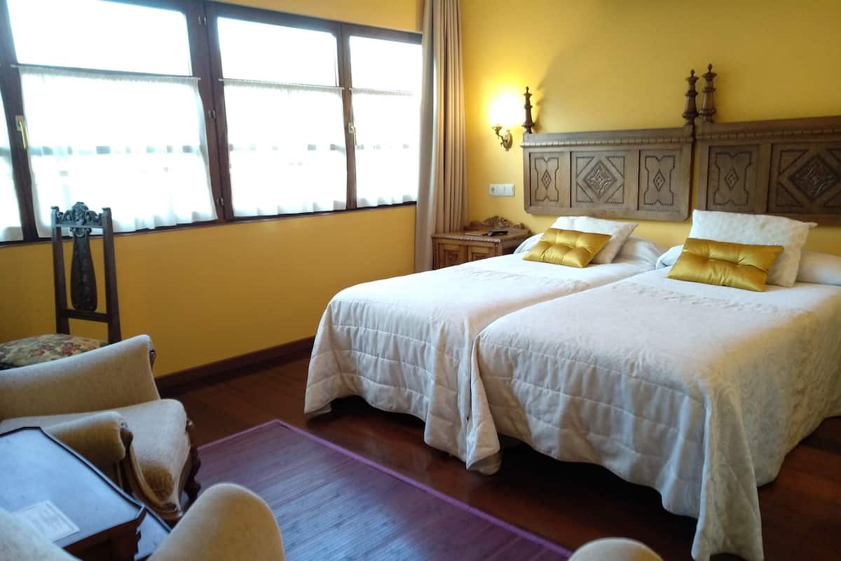 Une chambre d’hôtel avec deux lits, une chaise, une table de chevet et une fenêtre avec des rideaux.