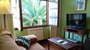 Un salon avec un canapé, une table basse, un téléviseur et une fenêtre donnant sur des palmiers.