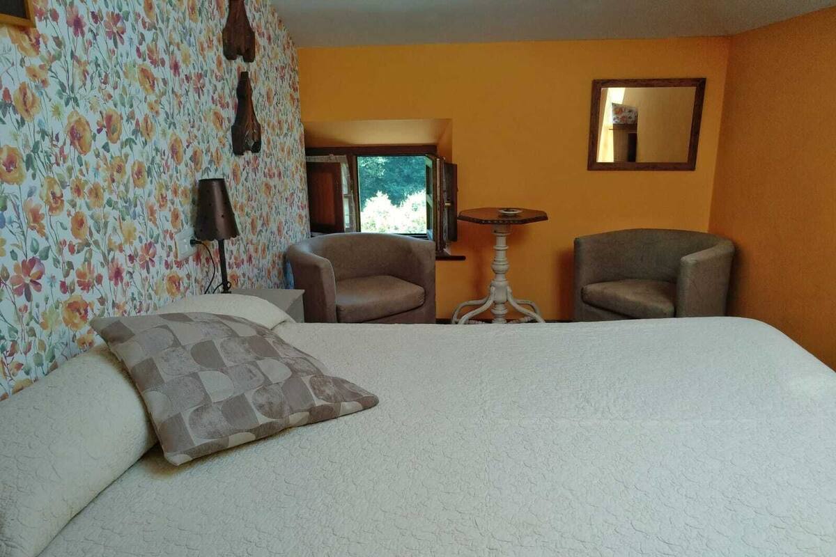 Une chambre d’hôtel avec un grand lit, deux fauteuils, une petite table et un papier peint à motifs floraux.