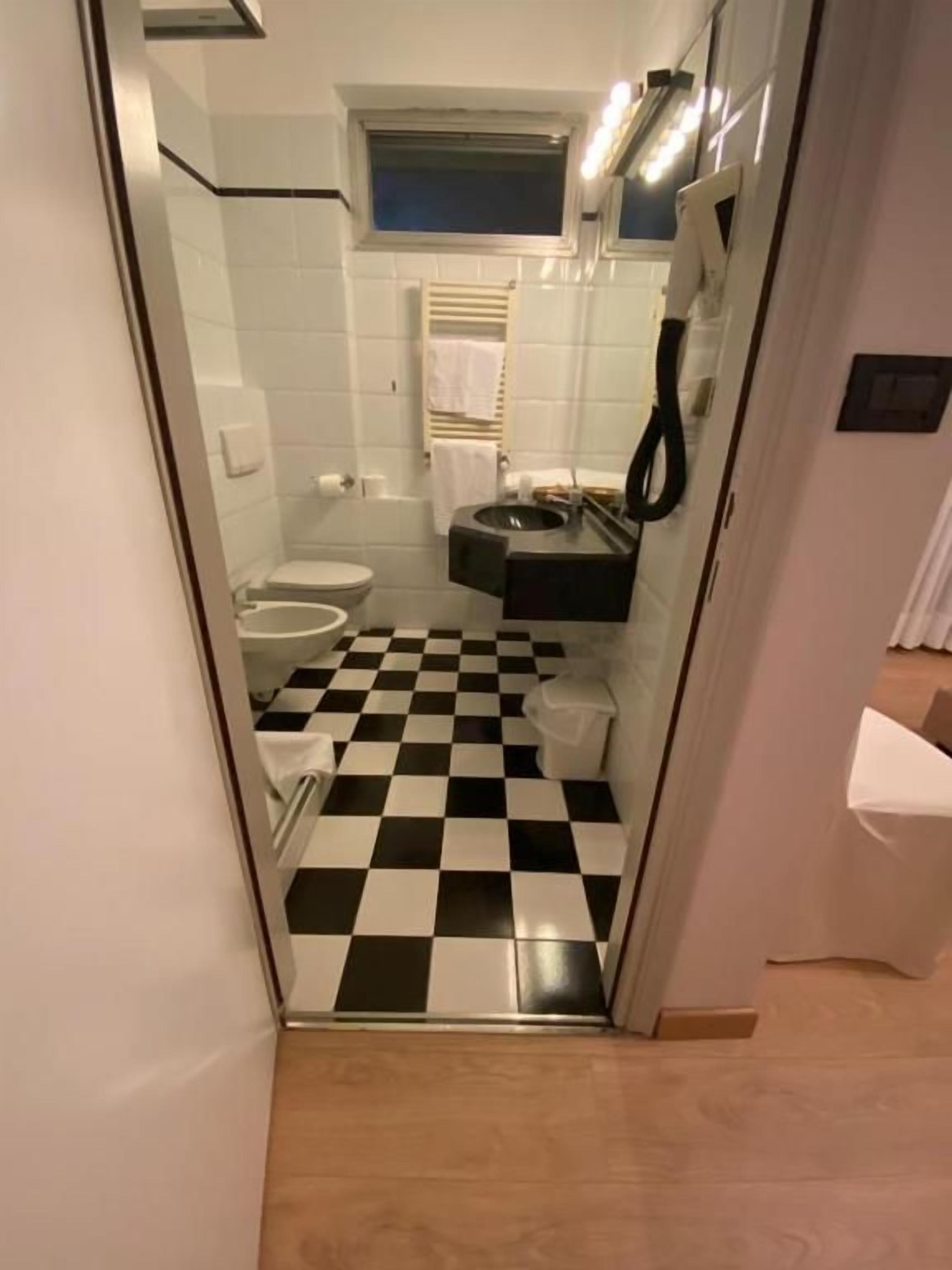 A bathroom with a checkered floor, a toilet, a sink, and a mirror.