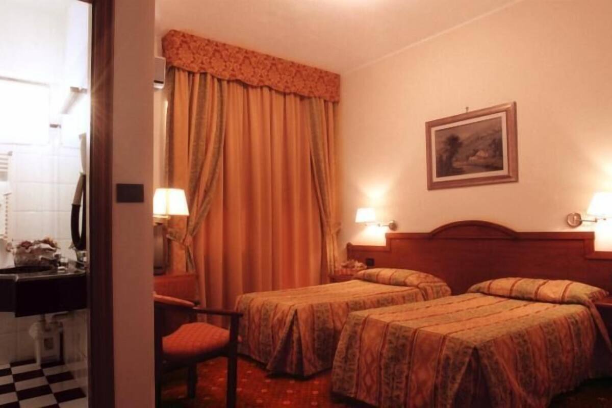 A hotel room with two beds, a bathroom with a checkered floor, and a painting on the wall.