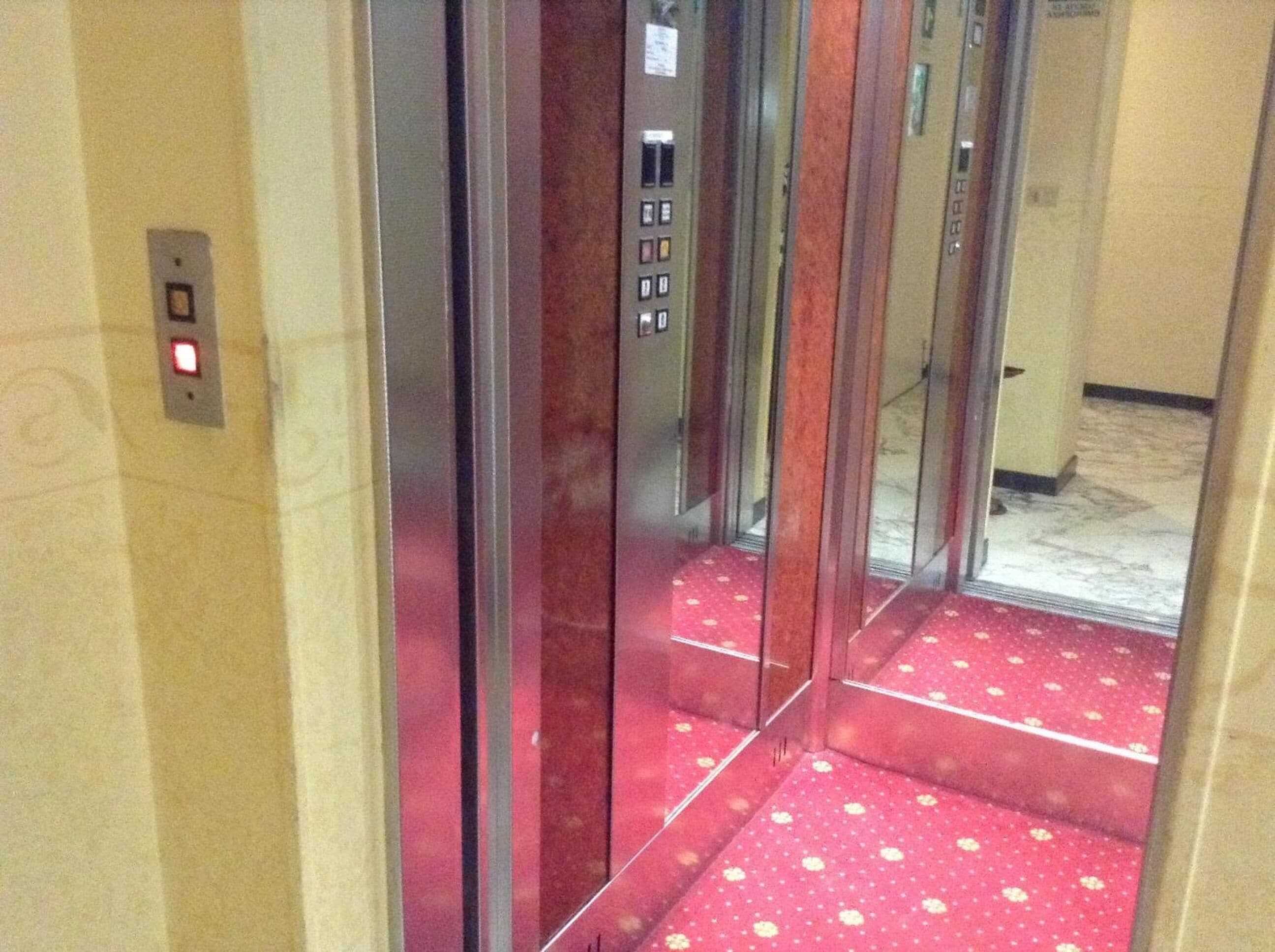 Interior de un ascensor con alfombra roja y un panel de control con botones.