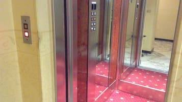 Interior de un ascensor con alfombra roja y un panel de control con botones.