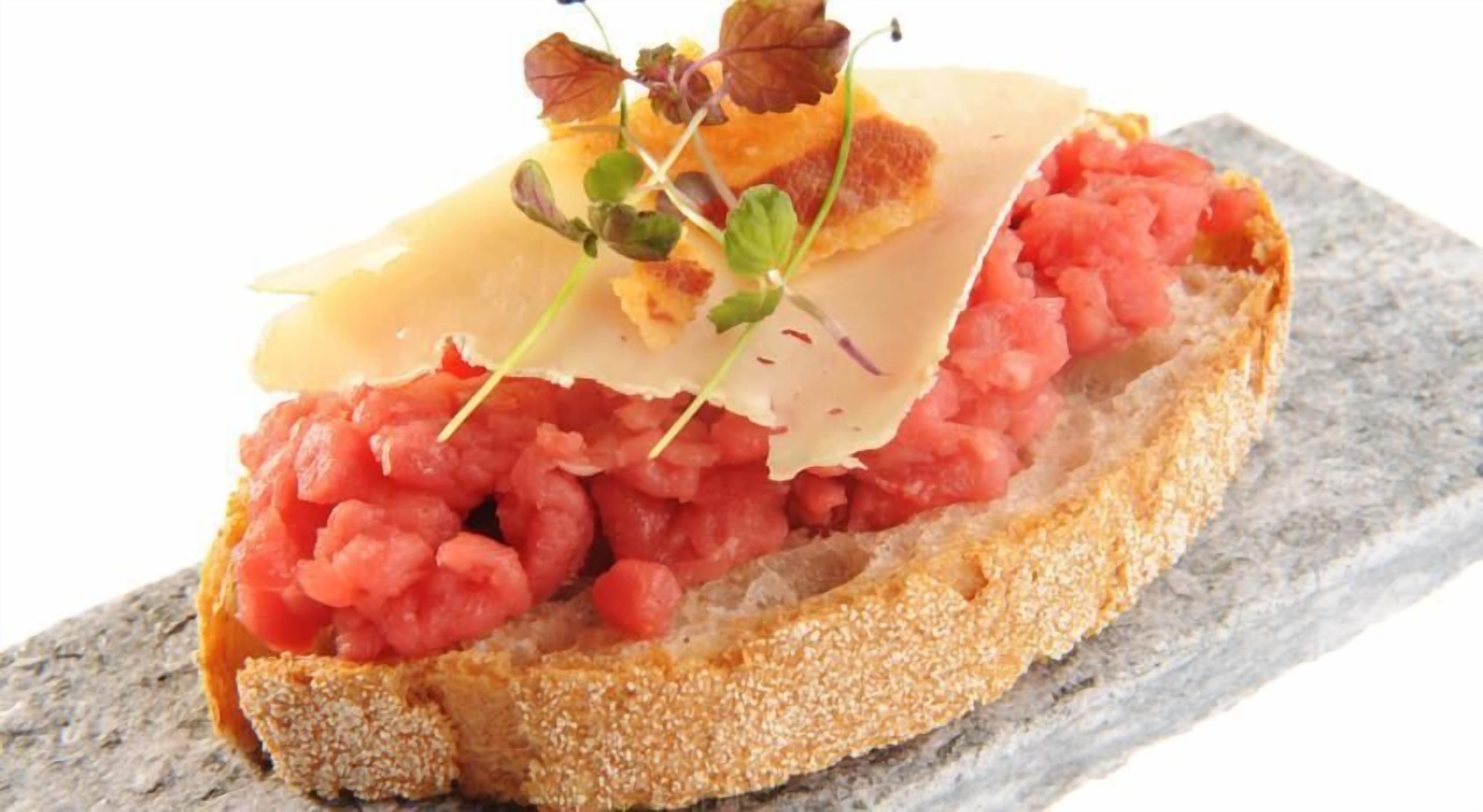 Una rebanada de pan cubierta con salsa roja, posiblemente una preparación a base de tomate, y una loncha de queso.