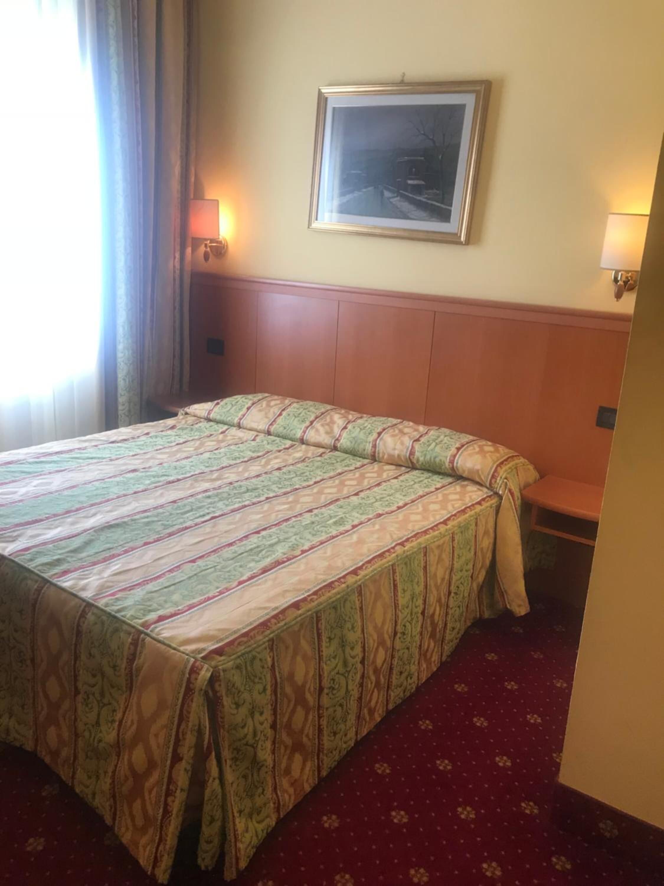 A hotel room with a large bed, a framed picture on the wall, and two wall-mounted lamps.
