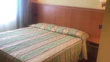 A hotel room with a large bed, a framed picture on the wall, and two wall-mounted lamps.