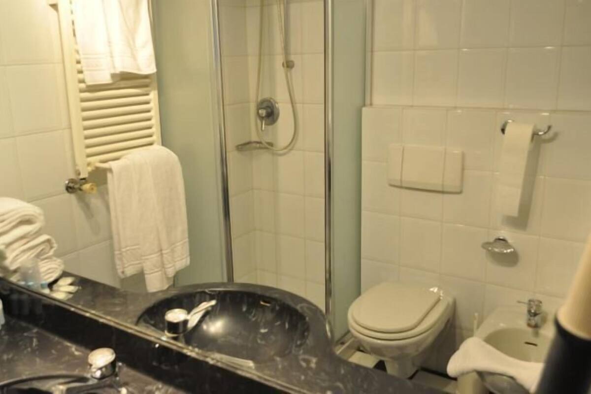 A bathroom with a glass-enclosed shower, a toilet, and a sink with a mirror.