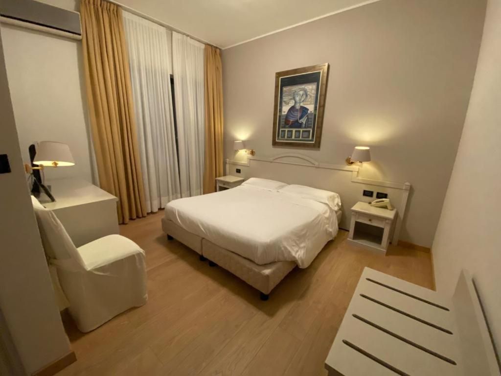 A hotel room with a bed, bedside tables, a chair, a desk, and a painting on the wall.