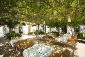 An outdoor dining area with tables and wicker chairs, surrounded by greenery and white walls. - Hotel Balneari Prats (Caldes de Malavella)
