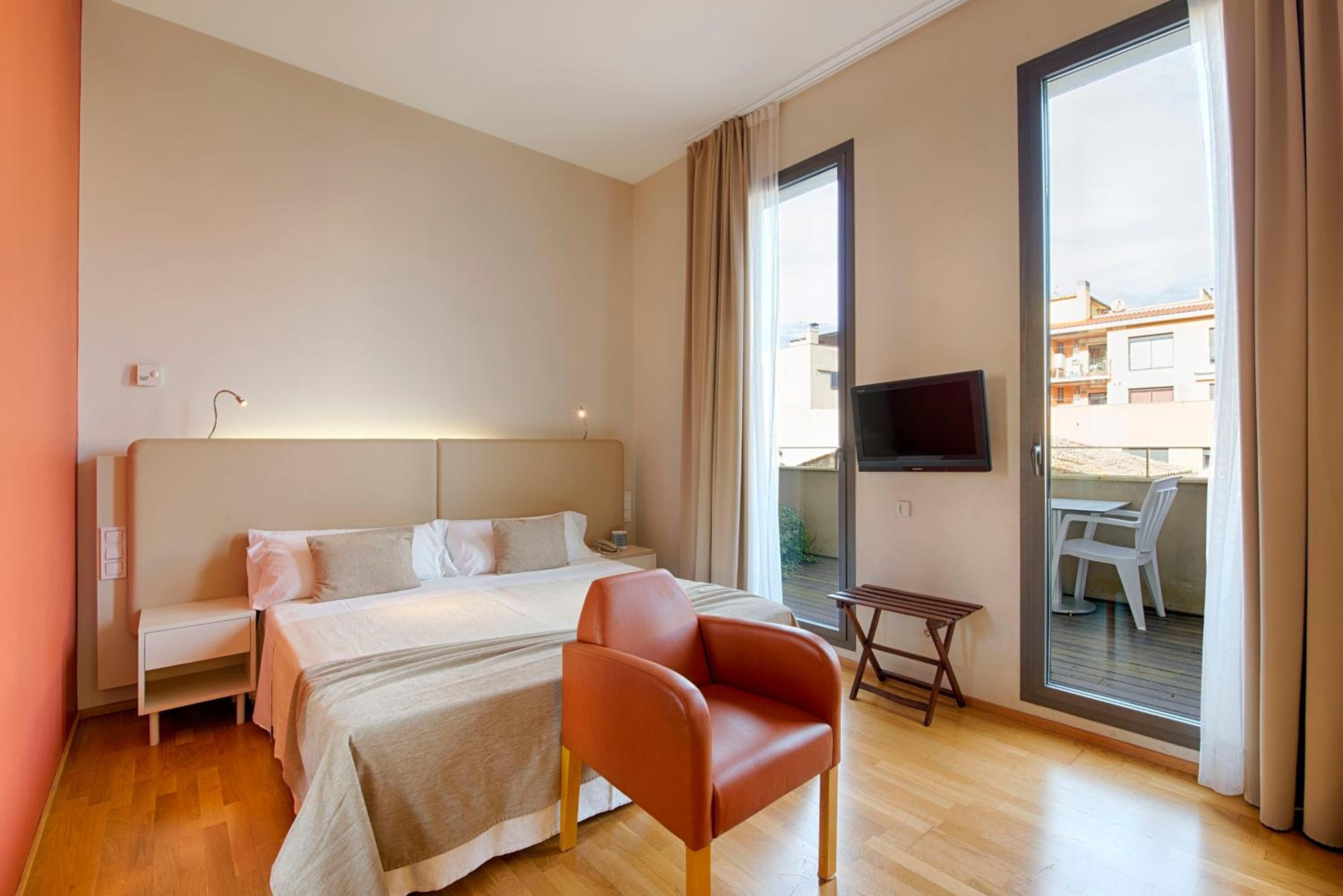 A modern hotel room with a large bed, a TV, a small table, and a chair.
