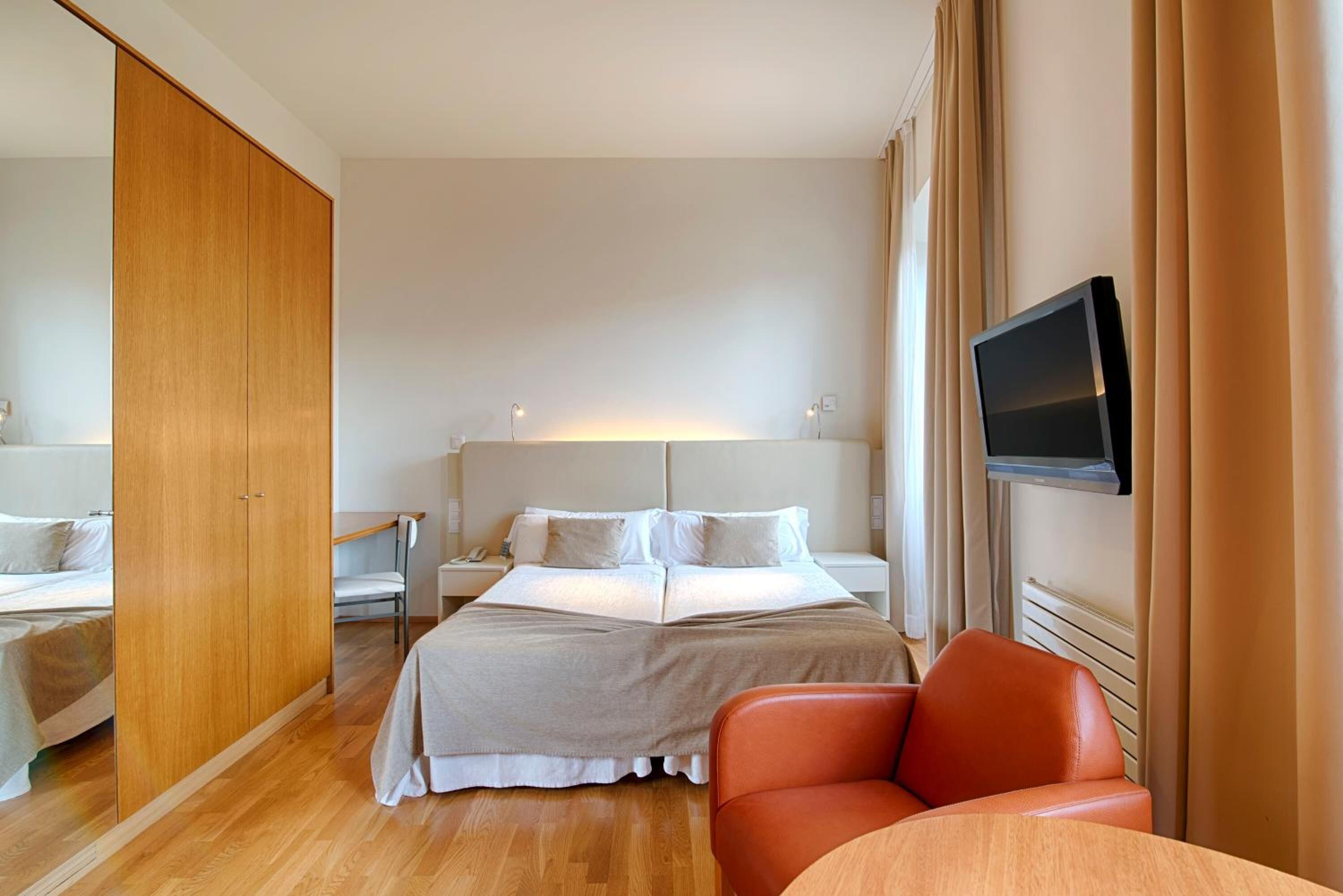 A hotel room with a bed, a TV, a desk, and a chair.