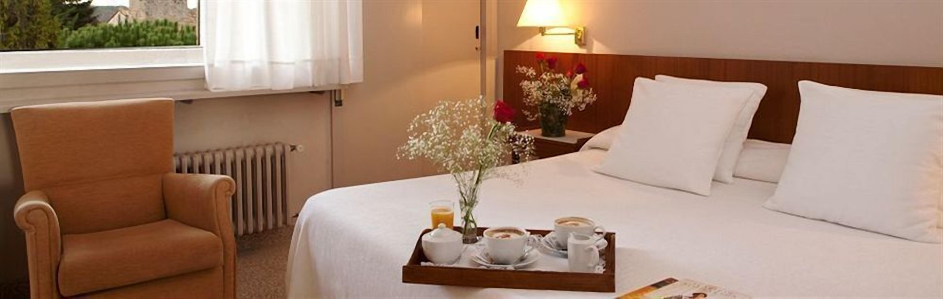 Ein Hotelzimmer mit Bett, Stuhl, Tablett mit Frühstücksangeboten und einem Fenster mit Vorhängen.