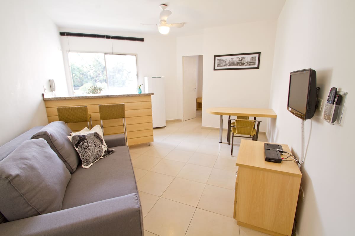 A compact living space with a sofa, a small dining table, a kitchenette, and a ceiling fan.