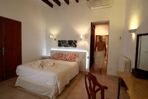 A bedroom with a bed, bedside lamps, a wooden chair, a table, and a mirror.