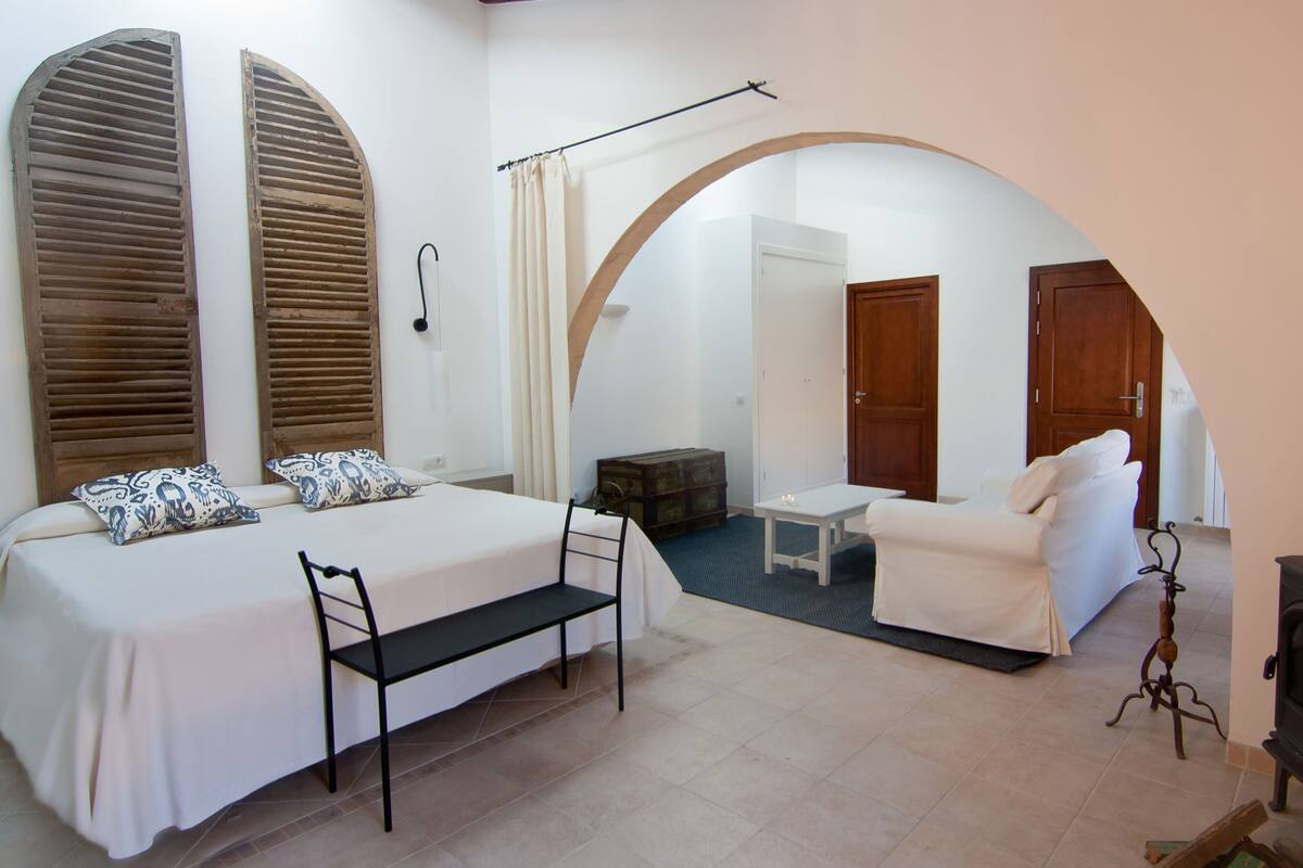A bedroom with a bed, bench, and a fireplace.