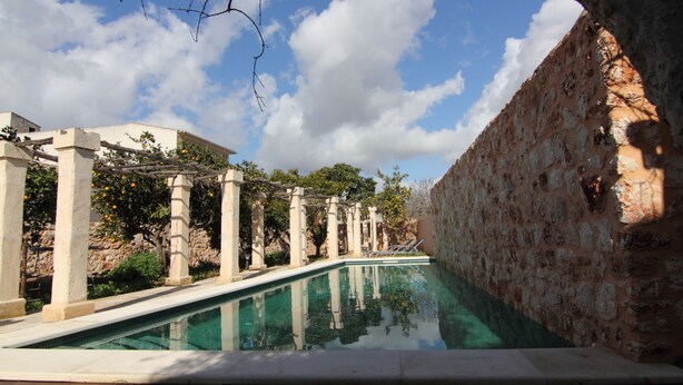 A pool with stone columns and a clear blue sky. - Petit Hotel Algaida  (Algaida)