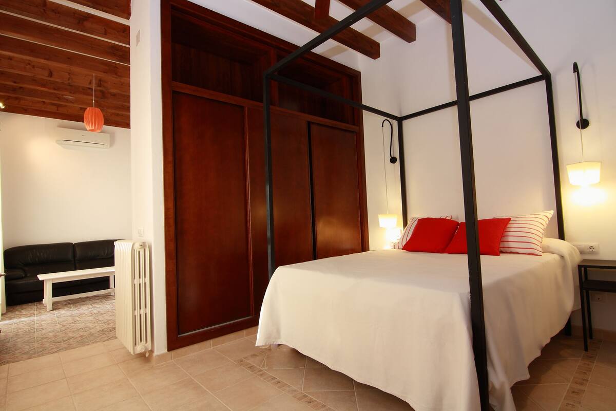 A bedroom with a four-poster bed, a wooden wardrobe, a white radiator, and a black bench.