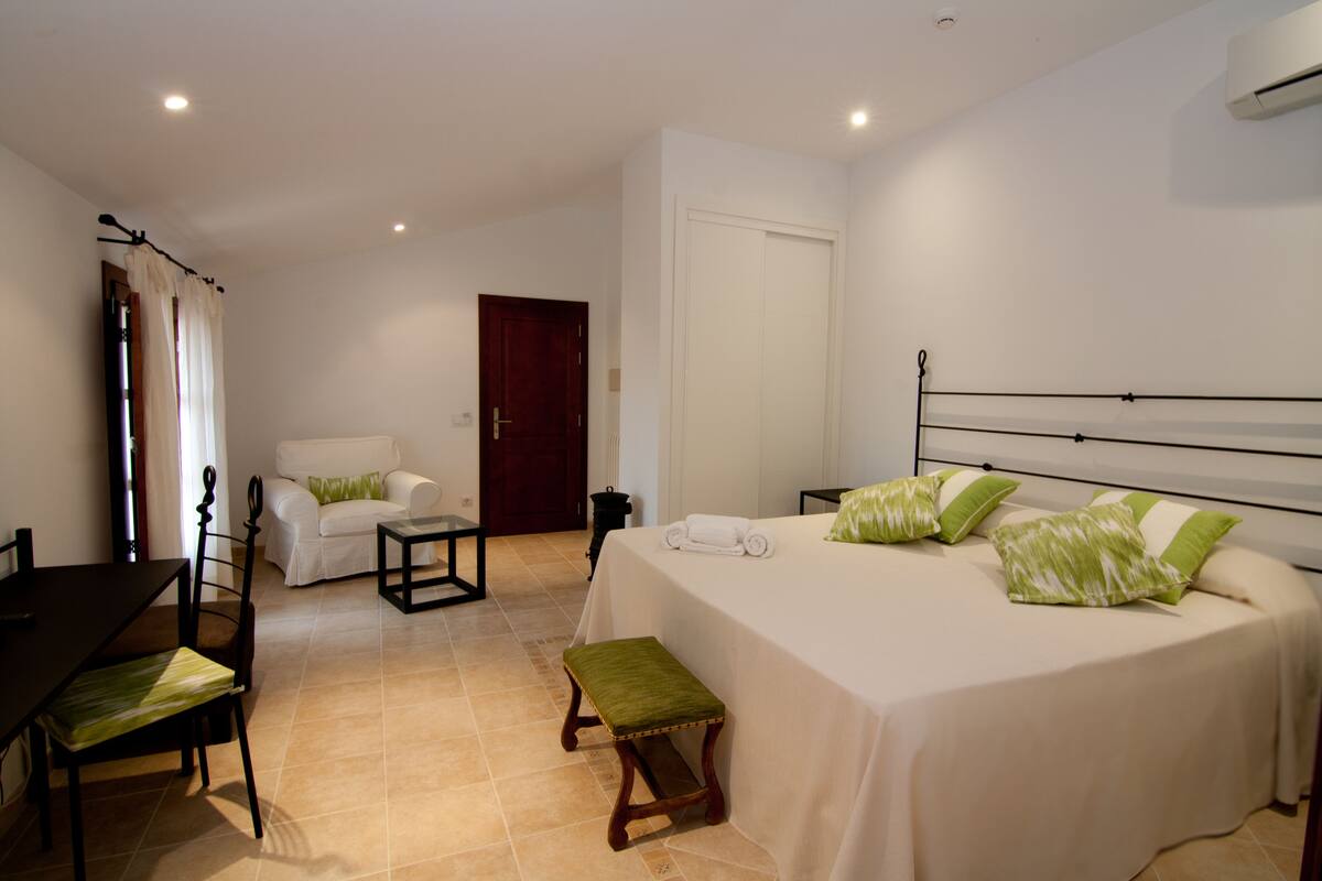 A bedroom with a bed, a chair, a table, and a door.