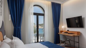 Habitación de hotel con cama, escritorio, silla, televisor y balcón con vista al mar.