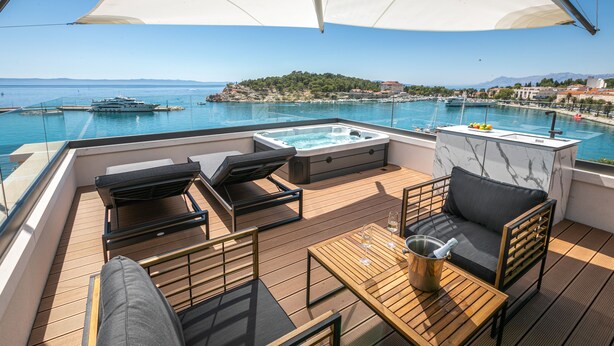 Una terraza con mobiliario exterior, bañera de hidromasaje y vistas al mar y a una isla distante.