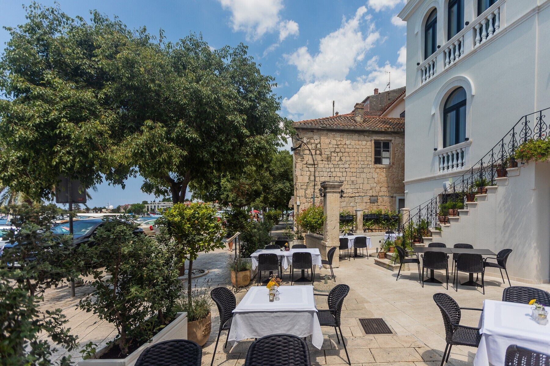 An outdoor dining area with tables and chairs, a stone building, and a view of the sea.