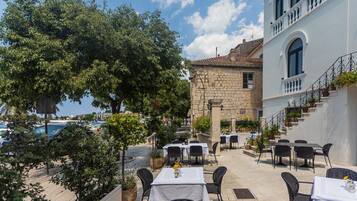 An outdoor dining area with tables and chairs, a stone building, and a view of the sea.
