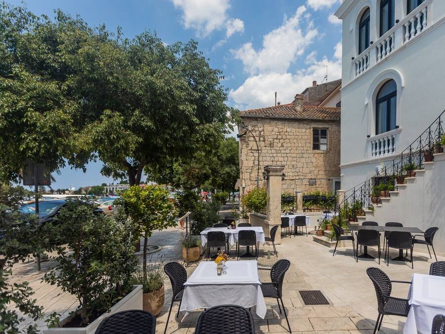 An outdoor dining area with tables and chairs, a stone building, and a view of the sea.