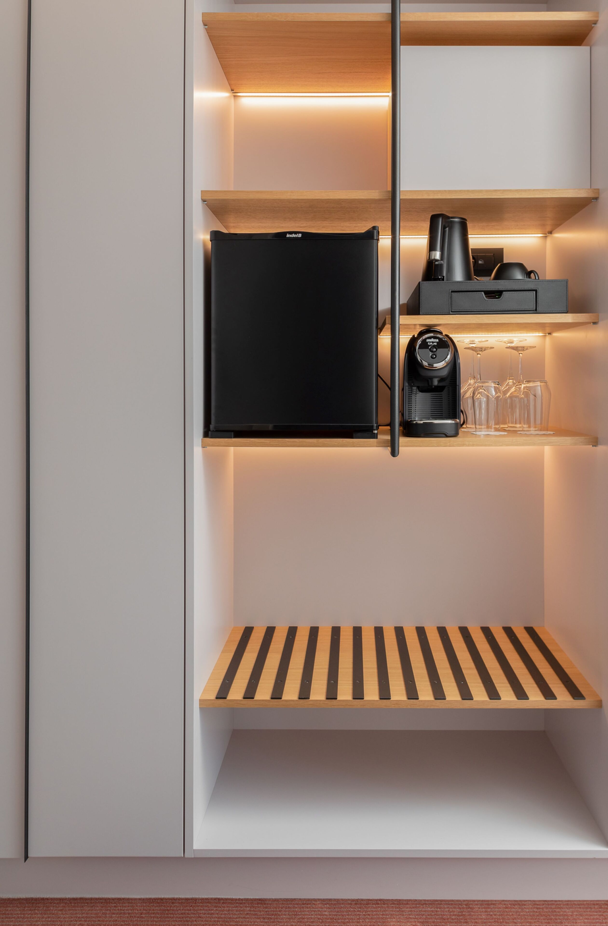 Una cocina moderna con electrodomésticos integrados, una cafetera y copas de vino en una estantería.