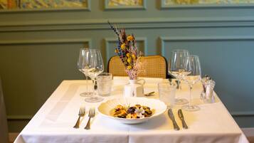 A dining table set with a white tablecloth, a bowl of food, and various glassware and cutlery.