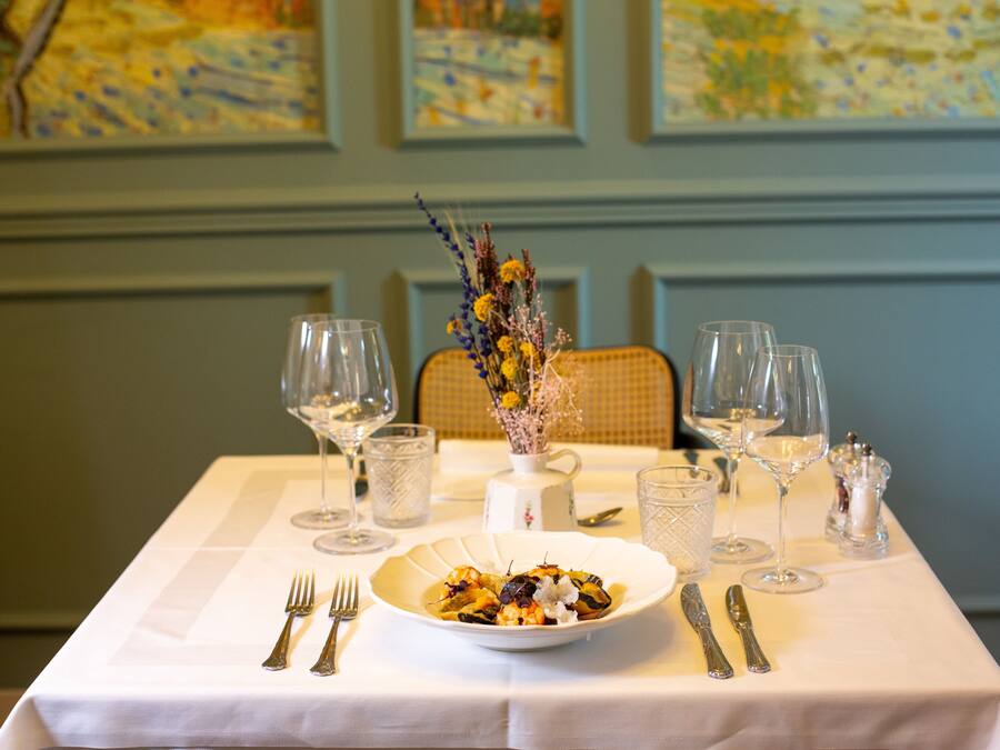A dining table set with a white tablecloth, a bowl of food, and various glassware and cutlery.