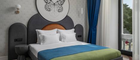 Une chambre d’hôtel moderne avec un grand lit, une tête de lit ornée d’une œuvre d’art représentant un papillon, une table de chevet et une vue sur l’extérieur.