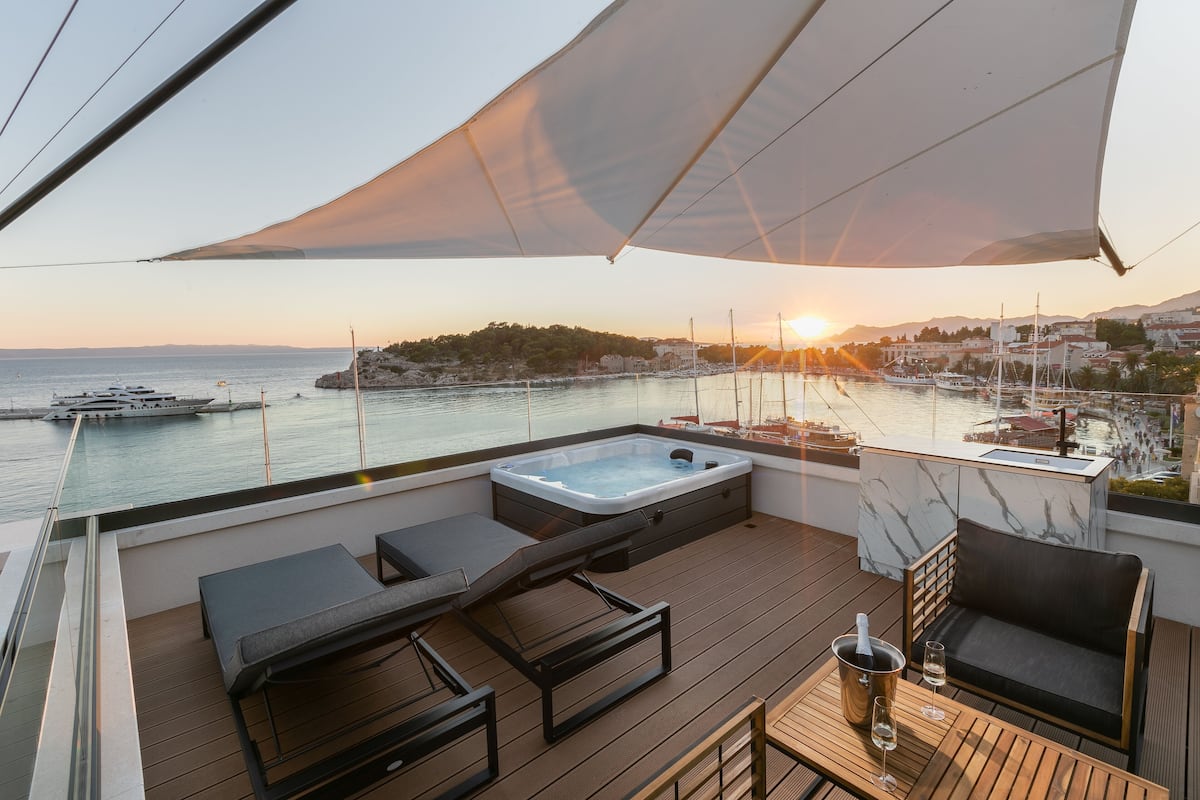 Een terras met een jacuzzi, lounge stoelen en een tafel met een fles en glas.