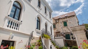 Un hotel con fachada blanca, varios balcones y una escalera que conduce a la entrada.