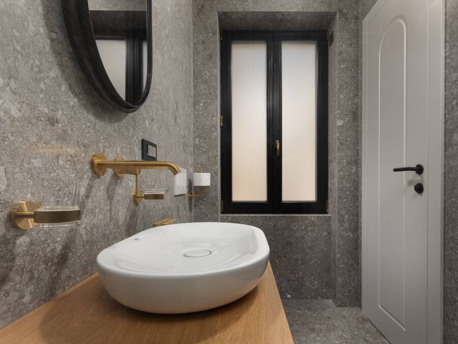 Un baño con un lavamanos ovalado grande, un espejo, un ventanal con vidrio esmerilado y una puerta.