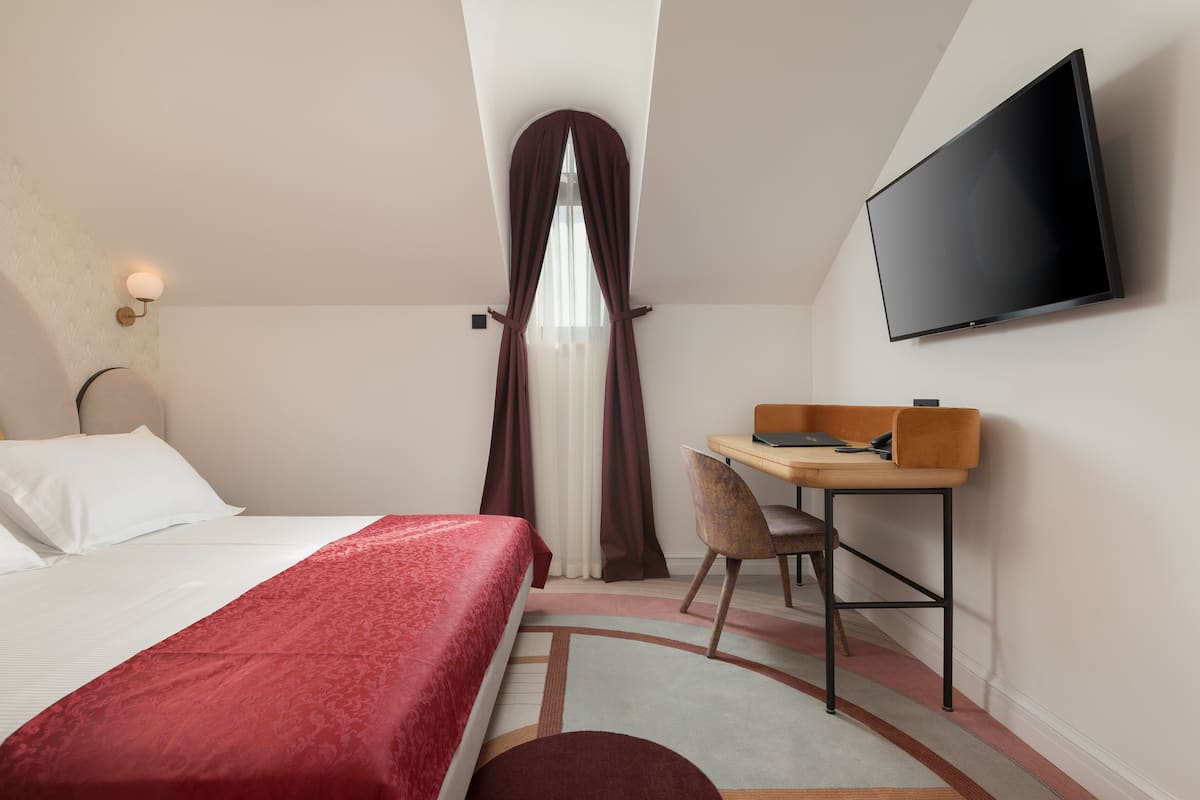 Een hotelkamer met een bed, een bureau, een stoel, een televisie en een raam met gordijnen.