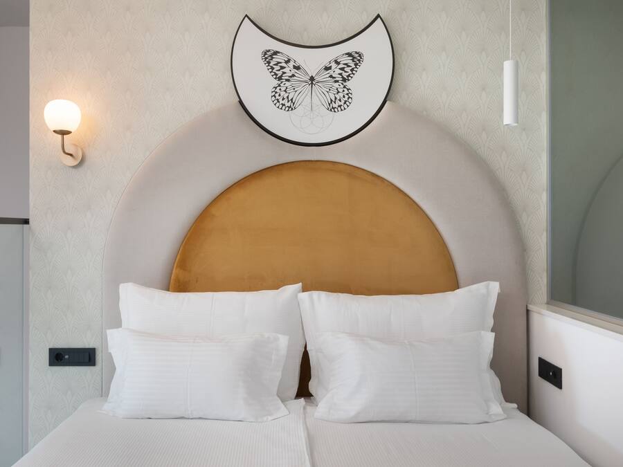 A neatly made bed with white linens and a large, rounded headboard.