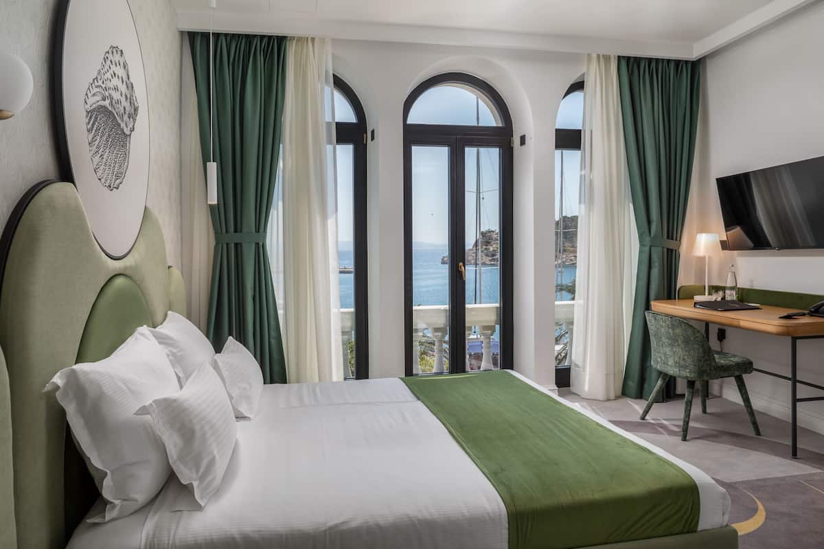 Een hotelkamer met een bed, een bureau, een stoel, een televisie en uitzicht op zee.
