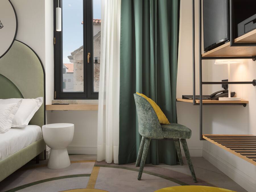 A modern hotel room with a bed, a chair, a toilet, and a window with curtains.