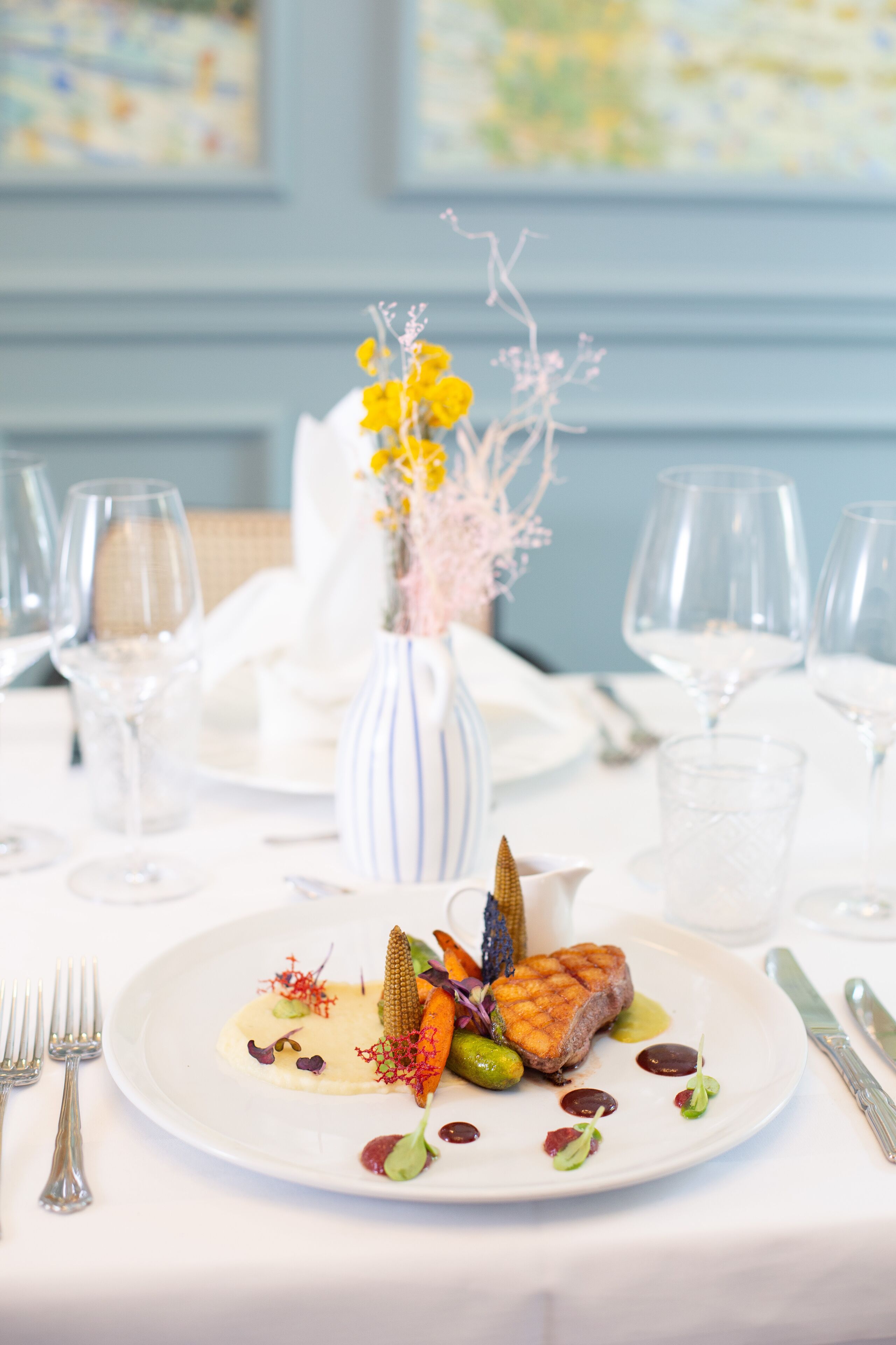 A dining table set with a white plate of food, wine glasses, and cutlery.