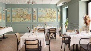 Un comedor con mesas dispuestas para una comida, rodeado de sillas y grandes cuadros en las paredes.