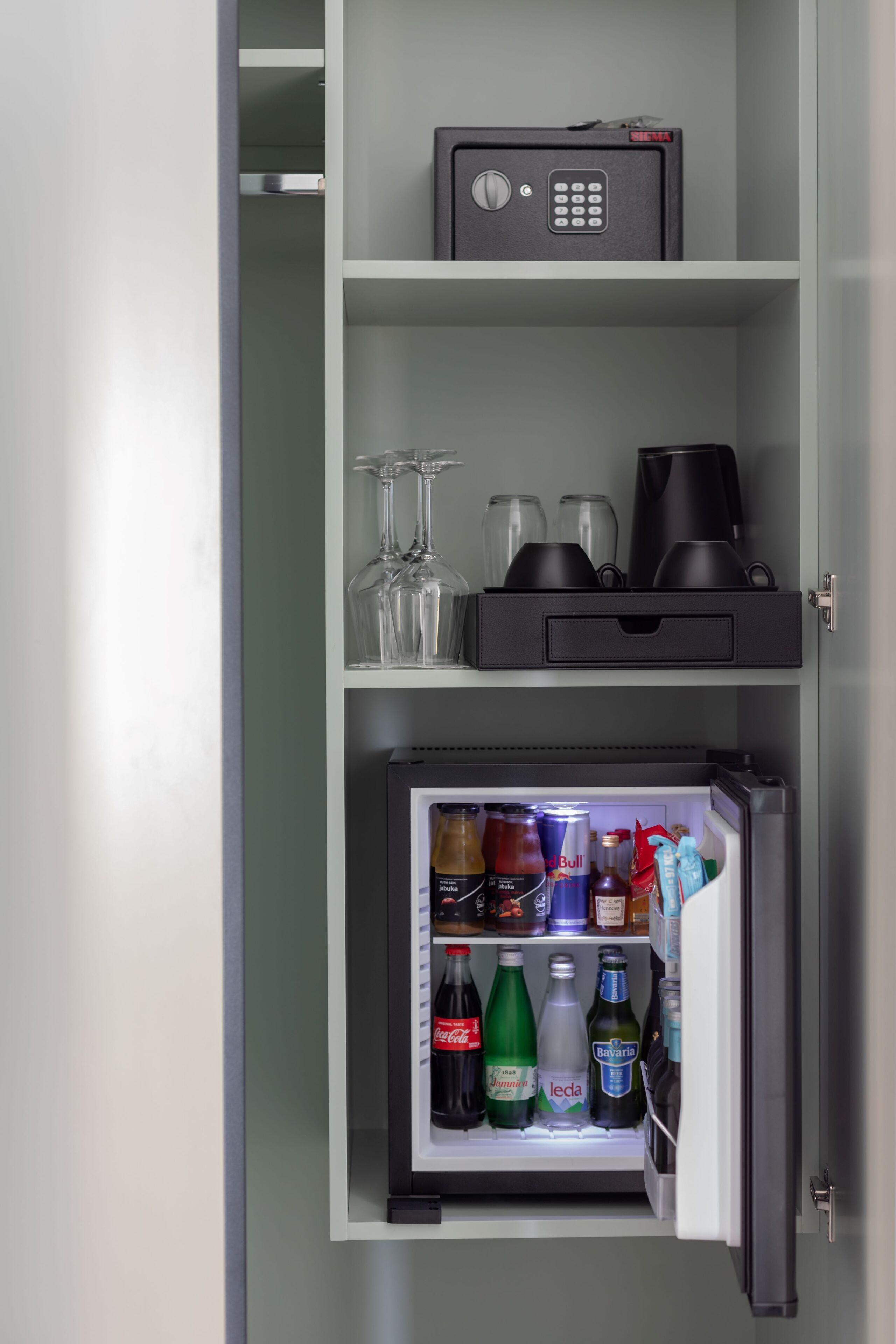 Eine Minibar mit Safe, Weingläsern und einer Auswahl an Getränken.