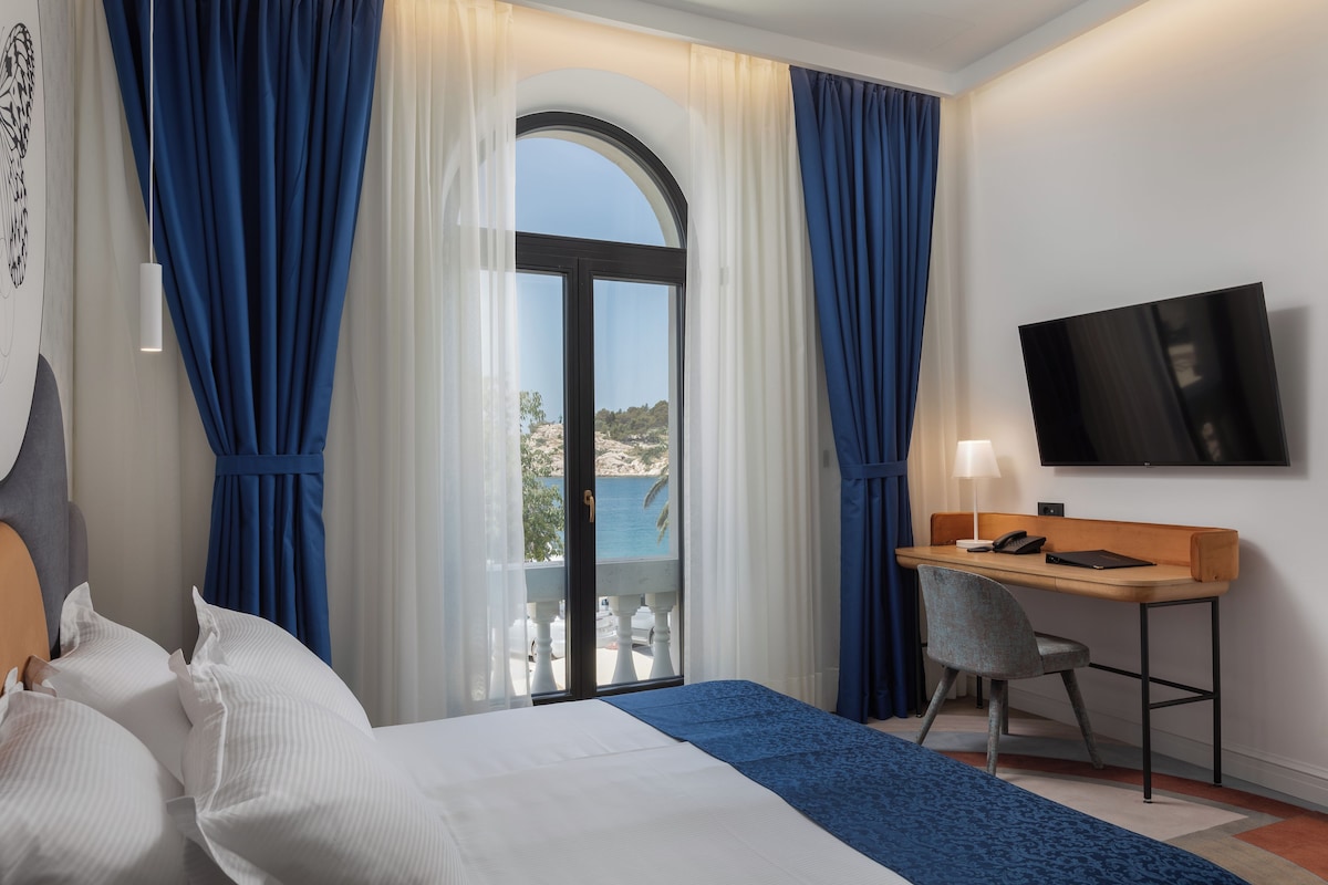 Une chambre d’hôtel comprenant un lit, un bureau, une chaise, une télévision et un balcon avec vue sur la mer.
