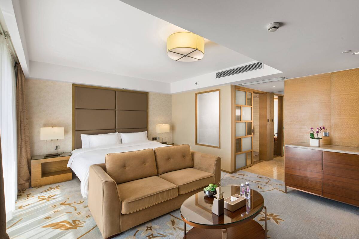 A hotel room with a bed, a sofa, a desk, and a lamp.