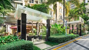 L’entrée d’un hôtel, avec un espace extérieur abrité aménagé en coin salon, un parasol rouge et une végétation luxuriante.