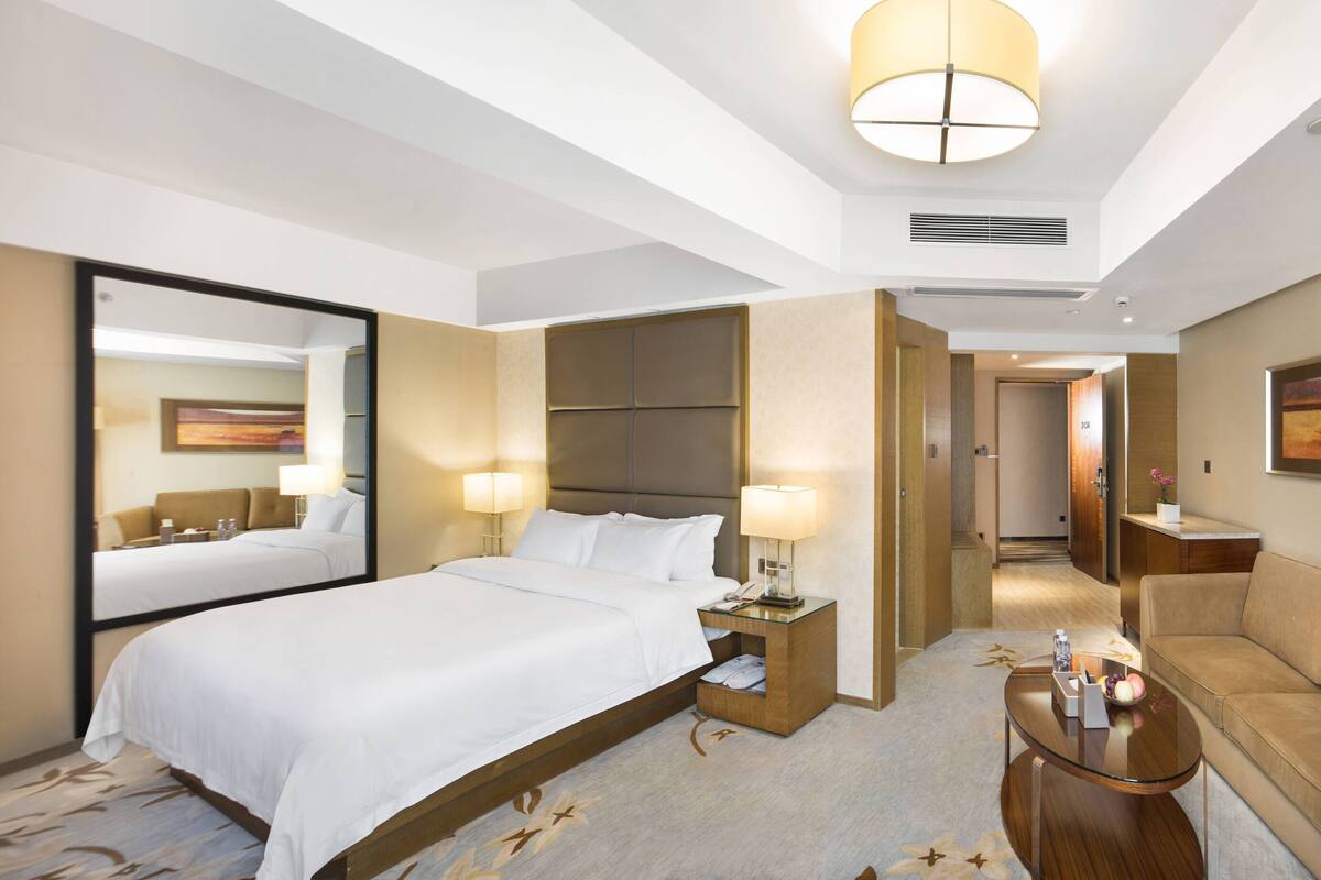 A hotel room with a bed, a sofa, a coffee table, and a large mirror.