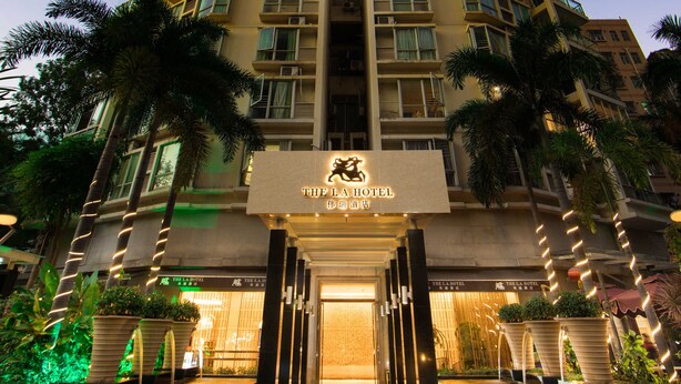 Un grand hôtel à l’entrée à carreaux, bordé de palmiers et doté d’une enseigne lumineuse.